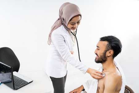 Muslim female doctor using a stethoscope examining prospective Hajj pilgrims on isolated backgroundの写真素材