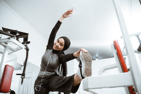 Attractive sports muslim girl smiles and looks at the camera while stretching her body in the gym,...