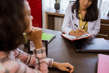 female doctor writing on paper and clipboard during consultation with a female patient against room backgroundの写真素材