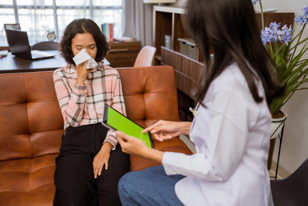 female doctor using a tablet while consulting a female patient sitting on a sofa