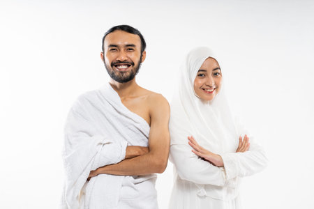 Couple wearing ihram clothes with folded hands gesture standing on isolated background