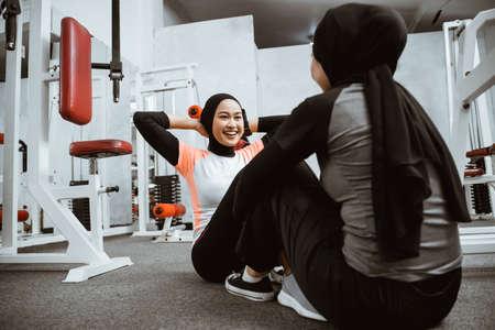 beautiful muslim woman sitting up exercise with partner at the gymの写真素材
