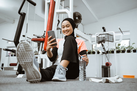 beautiful muslim sporty woman taking a break after exercising at the gym sitting on the floor and...