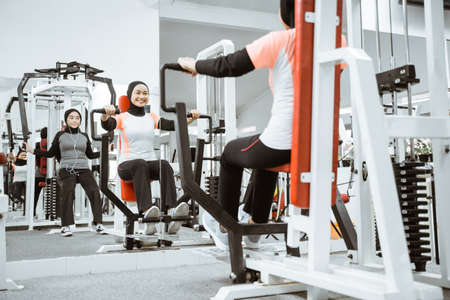 beautiful muslim asian woman using chest press machine during fitness at the gym with friendの写真素材
