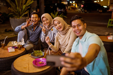 portrait of happy muslim friend enjoy having iftar dinner at traditional food stall sitting on the...