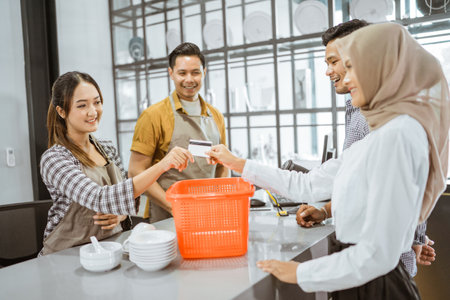Shop assistant accepts credit card from female customer at checkout at houseware storeの写真素材