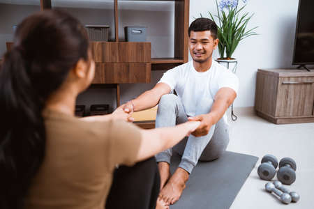 Asian fitness couple, man and woman exercising together at home doing yoga in livingroom facing each otherの写真素材