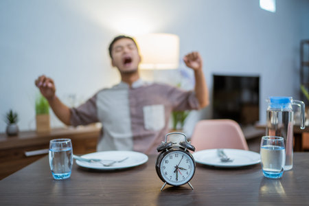 tired muslim male wake up early to have a morning breakfast on fasting month. sahur concept in...