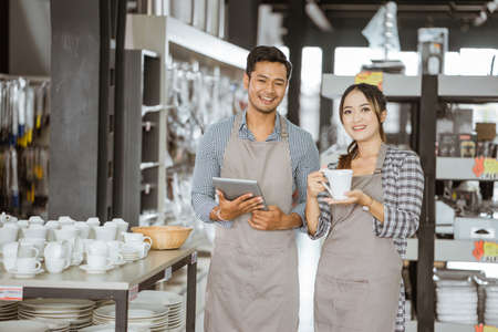 Boy and girl wearing aprons smiling while holding a pad and holding a cup in houseware storeの写真素材
