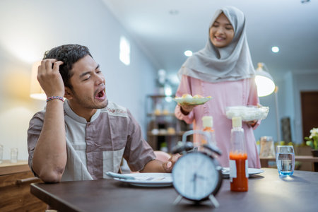 tired muslim couple wake up early to have a morning breakfast on fasting month. sahur concept in...