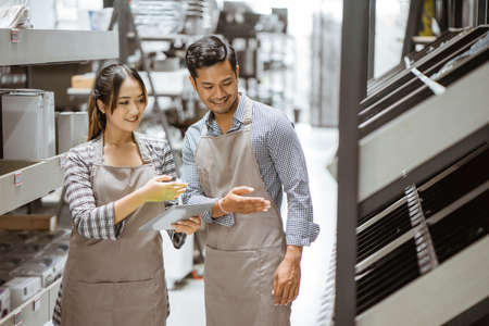 Boy and girl wearing aprons using a pad while checking items on shelves in houseware storeの写真素材