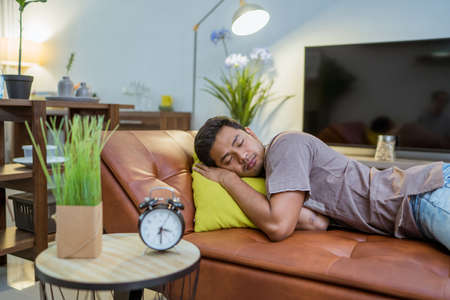 portrait of Handsome Young Asian man sleeping in bed with table clock at the foregroundの写真素材