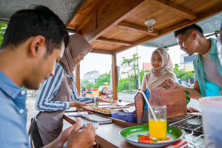 muslim couple ordering food to break fasting in traditional food market stall served by the seller