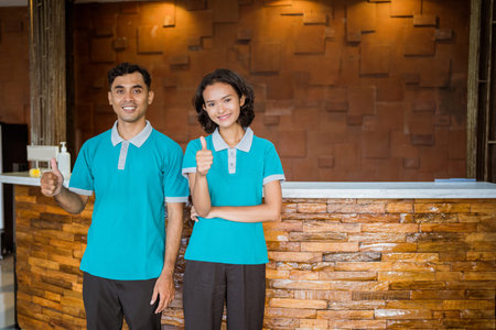 two janitors wearing turquoise uniforms smiling while standing with thumbs up in hotel lobby