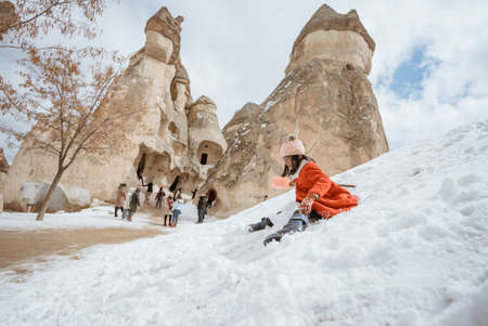 happy little girl in red sliding on a pile of snow in pasabag valley cappadociaの写真素材