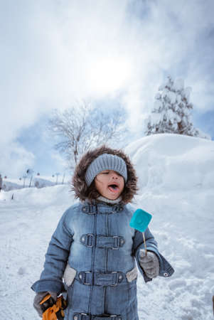 cute kid portrait close up while enjoying lollipop outside during snowy winterの写真素材