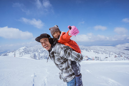 father giving piggyback ride to his daughter while playing outside in the snow