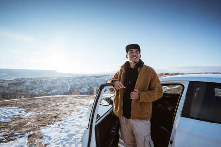 portrait of young asian man on his adventure going to beautiful hill in cappadocia in winter by his carの写真素材