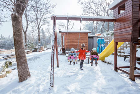 girl help swinging her brother and sister during playing in snowy playgroundの写真素材