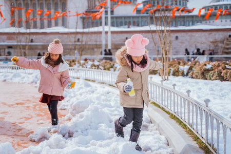 two little girl playing with snow in city square with the mosque in the backgroundの写真素材