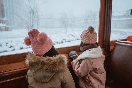 two asian little girl enjoy riding a tram during winter snow and looking at the windowの写真素材