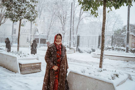 muslim mature woman standing in the middle of snow fall rain smiling to cameraの写真素材