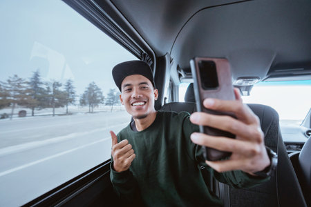 young asian male making a video call and selfie during his way out. man using mobile phone while travelling by a vanの写真素材