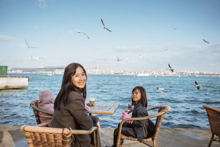 mother sitting on the side of bosphorus with her kids having some meal while enjoying the view with...