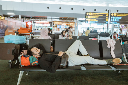 tired young man laying on a bench at the airport terminalの写真素材