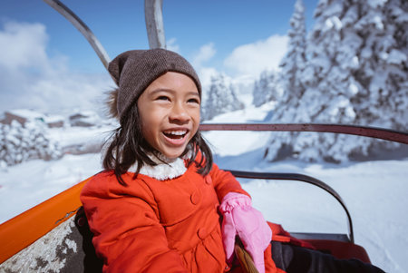 portrait of excited young girl riding a ski lift going up on top of the snowy mountainの写真素材