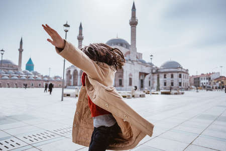 back portrait of happy kid dancing in the square of konya with mosque at the backgroundの写真素材