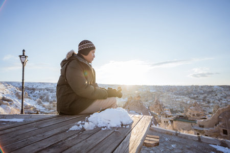 portrait of relaxed man sitting and enjoying the view of cappadocia in winter cover with snowの写真素材