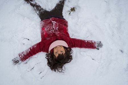 little girl laying on snow outside in the winter dayの写真素材