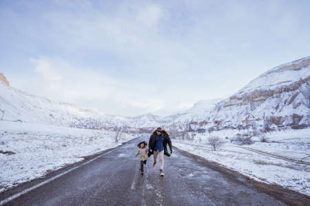 dad and daughter walking on empty street holding hand with majestic view of snowy valleyの写真素材