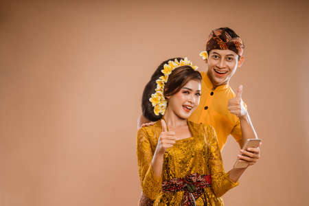 excited young balinese couple while using mobile phone over isolated backgroundの写真素材