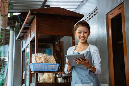 smiling saleswoman wearing apron standing holding a pad with chicken noodle cart backgroundの写真素材