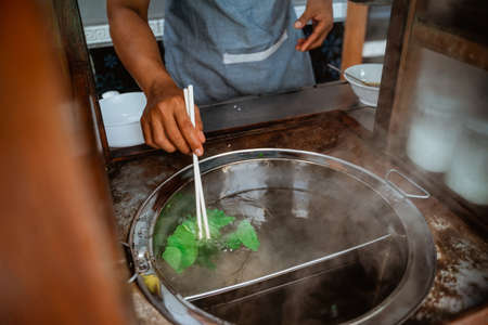 close up of mans hand boiled vegetables when prepare chicken noodle dish on the cartの写真素材