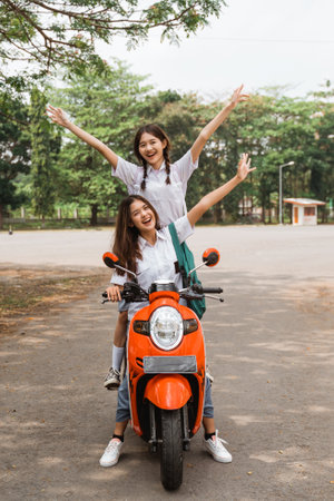 Two high school girls riding motorbikes standing while celebrating graduation on the streetの写真素材