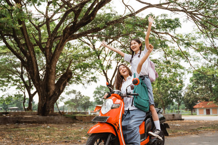 Two naughty high school girls ride on a reckless motorbike while celebrating graduation on the streetの写真素材
