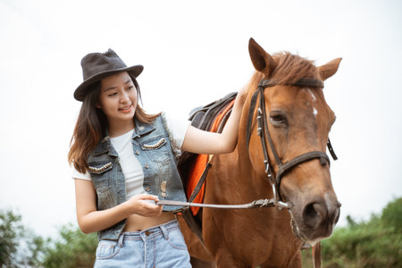 beautiful asian cowboy girl standing beside horse on outdoor backgroundの写真素材