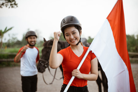 beautiful asian woman holding Indonesian flag with fist on background of man beside horse