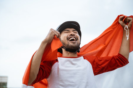 excited male athlete wearing a helmet carrying the Indonesian flag against a white sky backgroundの写真素材