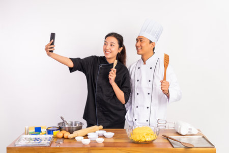 two chefs smiling while selfie holding spatulas standing near table on isolated backgroundの写真素材