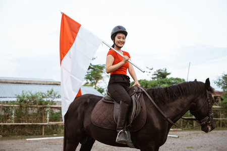 woman in a helmet riding a horse carrying the red and white Indonesian flag on the field background