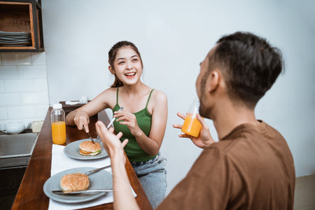 attractive young girl chatting with young man at breakfast at dining room tableの写真素材