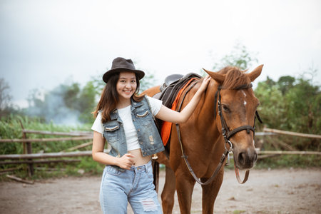 beautiful asian cowboy girl standing beside horse on outdoor backgroundの写真素材