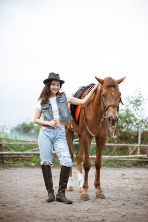 attractive asian cowboy girl standing beside horse on outdoor backgroundの写真素材