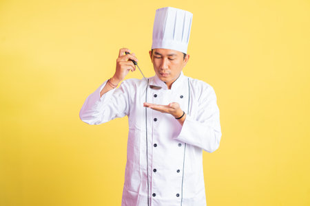 Asian male chef tasting hot food with a ladle on isolated backgroundの写真素材
