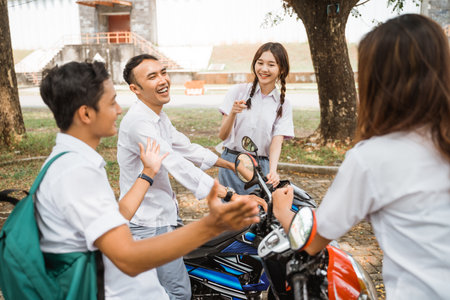 Group of Asian high school students chatting and joking when one rides a motorbikeの写真素材