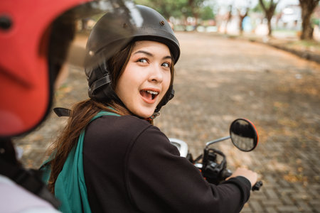High school students wearing helmets and jackets looking back chatting while riding motorbikes...